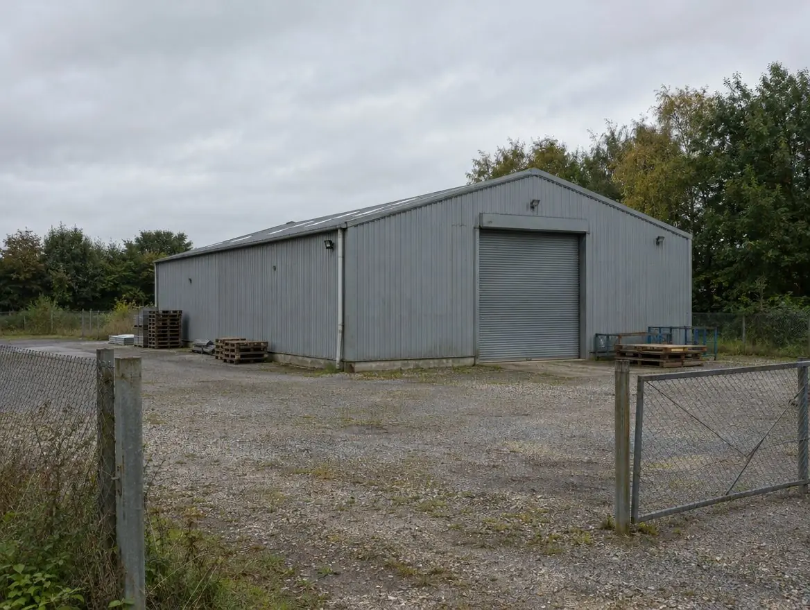 Redundant small industrial yard with a grey steel shed, gravel yard and chain-link fence