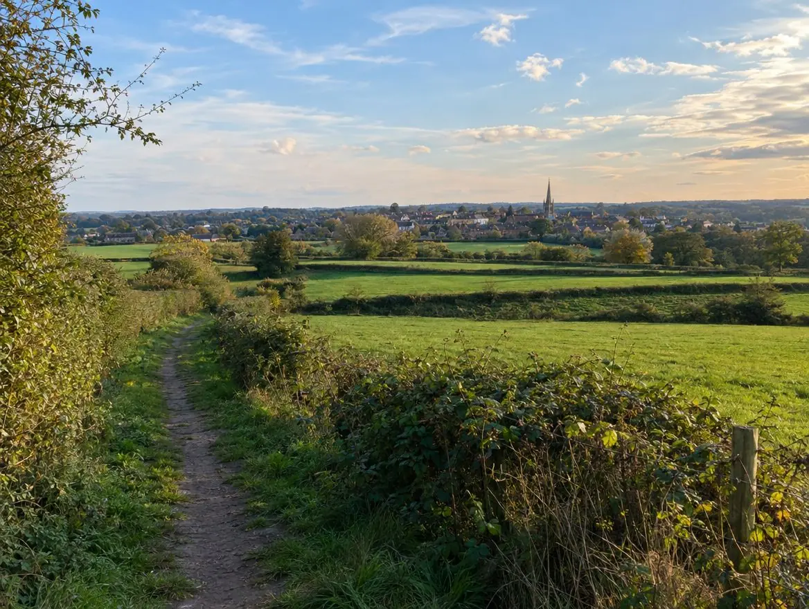 Green fields and a footpath on the edge of a market town with a church spire on the horizon