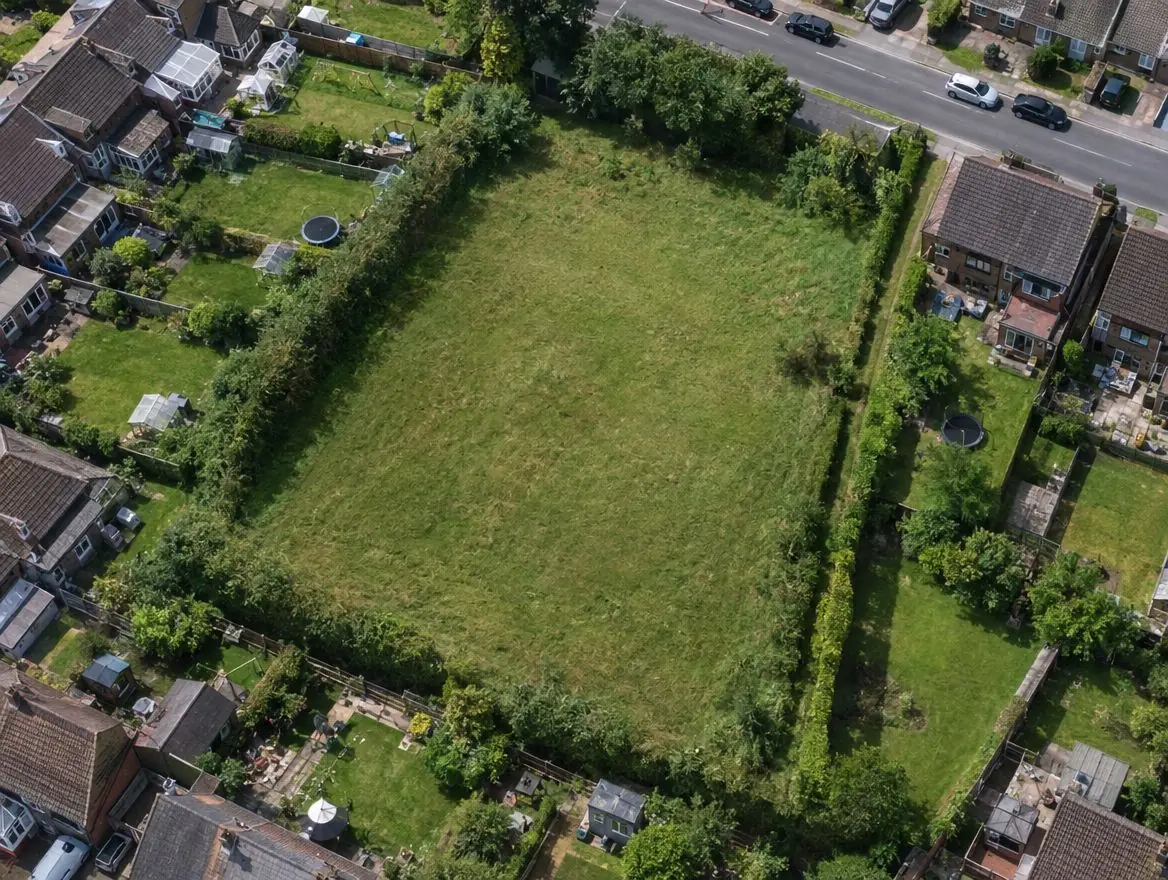 Aerial view of a grass field enclosed by gardens with only a narrow strip leading to the road