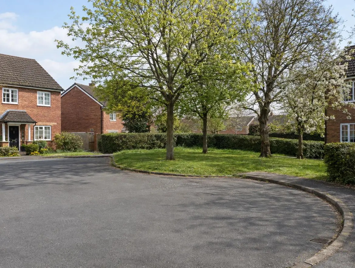 Small grassy corner plot with mature trees at the end of a cul-de-sac of brick houses